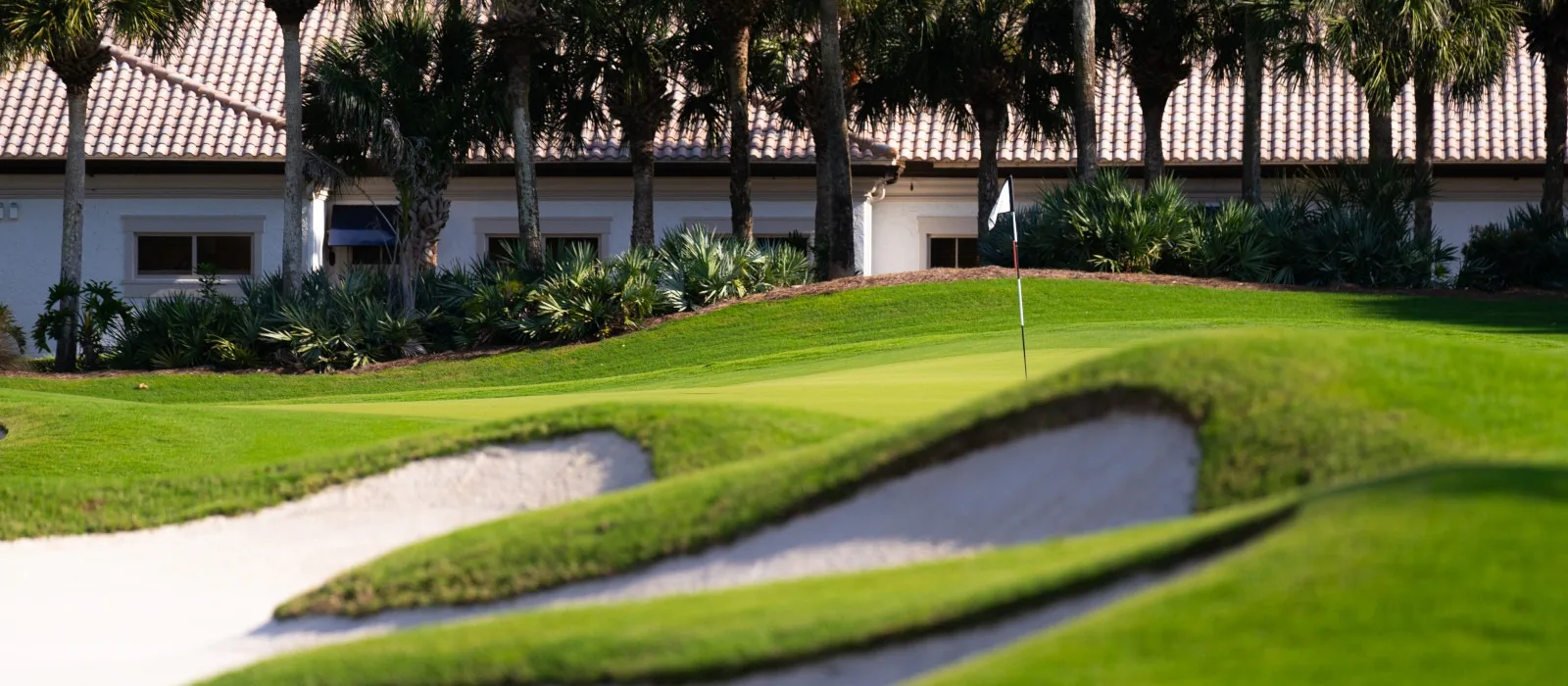 Golf green and bunker with clubhouse beyond at The Colony (official club site).