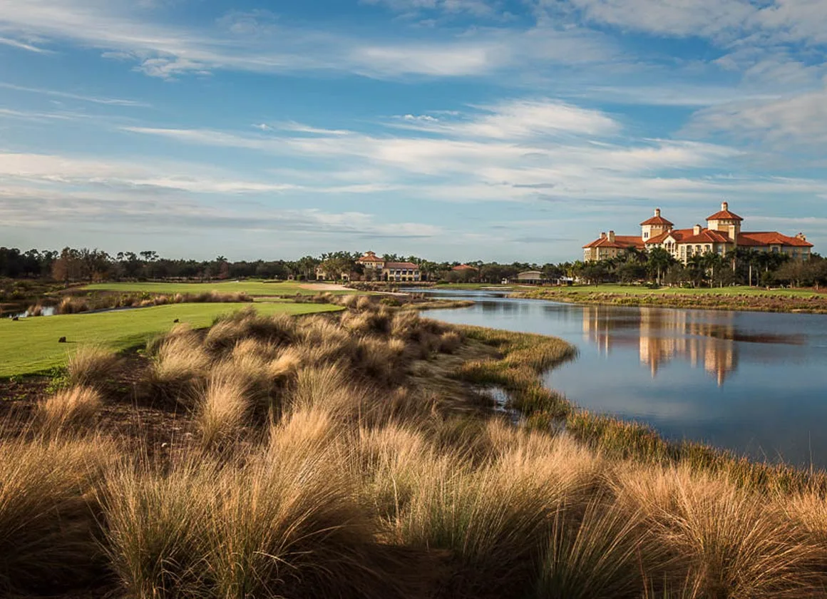 View across a lake lined with native grasses toward the clubhouse and resort at Tiburon, Naples.